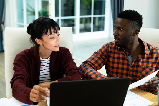 Multiracial young couple discussing household expense budget over laptop and bills at home