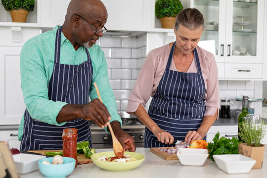 Senior multiracial couple preparing food together in kitchen at home