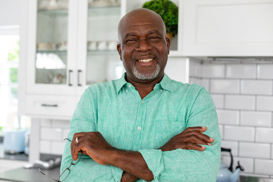 Portrait of smiling african american senior man with arms crossed standing in kitchen at home