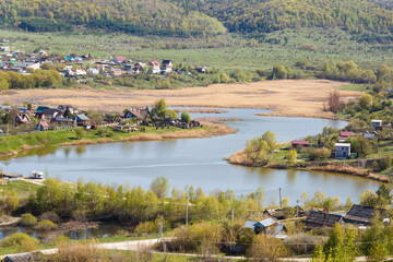 Fototapeta na wymiar The concept of a healthy lifestyle. View of the village with a lake at the foot of the mountain in early May. Life in the countryside away from civilization