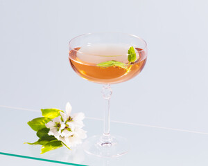 A Glass of natural apple cider with mint and apple blossoms on a glass shelves on a blue background. A wine glass with a refreshing Low-alcohol drink. Summer beverage. Fruit wine.