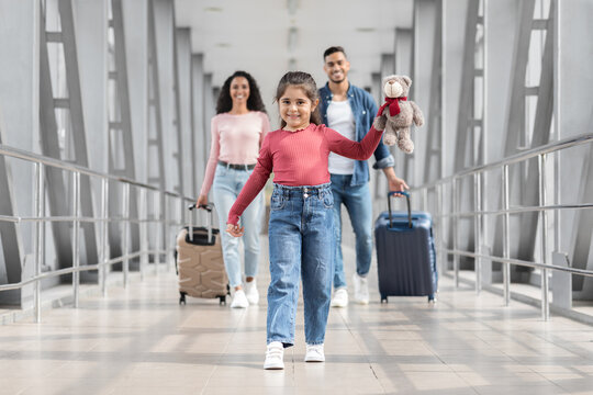 Portrait Of Joyful Cute Middle Eastern Girl Walking At Airport With Parents