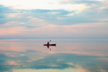 Fototapeta na wymiar a boy swims along the estuary in a kayak during a beautiful sunset