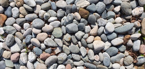 Scattering of rounded stones lying on the ground in sunlight. Mobile photography. Background for design, decor and texture.