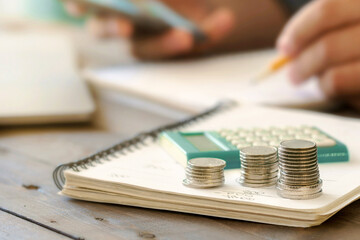 Stack of coins with a calculator on a wooden table close up. Man examining home finance concept