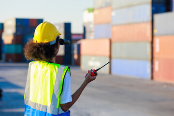 Back view black female dock worker control loading containers box from cargo at warehouse container...