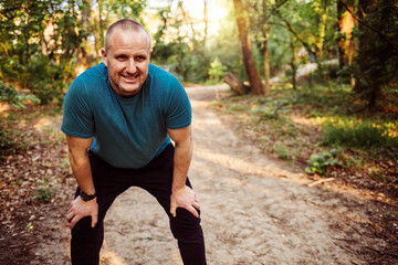 Portrait of athletic mature man after run. Handsome senior man resting after jog at the park on a sunny day. Sweaty multiethnic man listening to music while jogging.