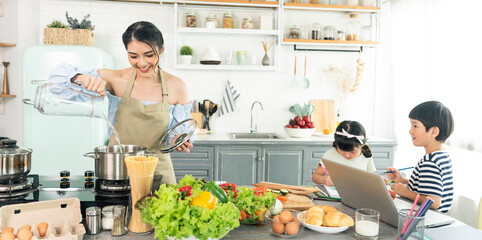 Asian young single mother making food while taking care child in kitchen. home school and single...