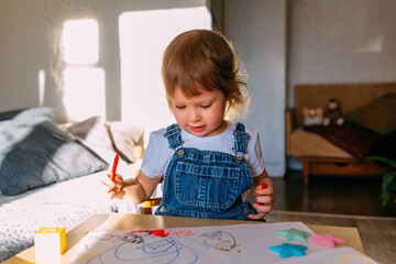 Small child at home at the children's table draws with felt-tip pens.