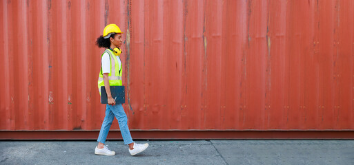 Black female dock worker walking go to work at warehouse container yard. Marine and carrier insurance concept. cargo shipping container box in logistic shipping yard