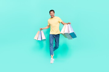 Full size photo of nice brunet guy run with bag wear t-shirt jeans shoes isolated on teal background