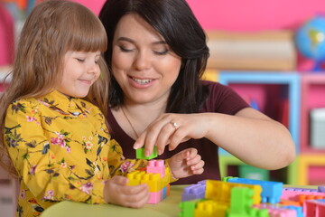 Little girl and mother playing with colorful plastic blocks