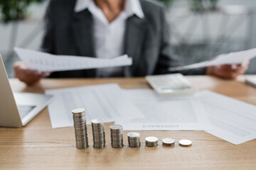 stacks of silver coins near cropped financier working with papers on blurred background.