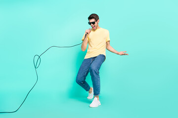 Full length photo of funny brunet young guy sing wear glasses t-shirt jeans footwear isolated on turquoise background - obrazy, fototapety, plakaty