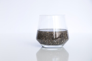 Edible chia seeds from the Salvia hispanica plant. Very healthy functional food to use in various recipes. Glass cup containing the hydrated seeds. Image seen from the front on white background.