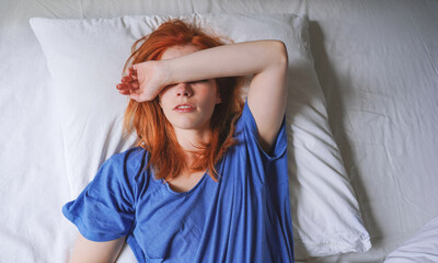 woman lying in bed with migraine and sensitivity to light covering her eyes