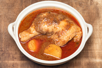 Curry chicken with coconut in bowl on wood background.