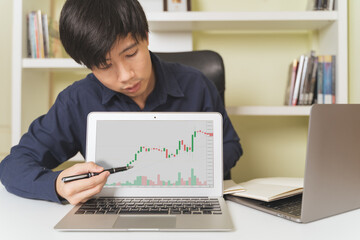 Asian trading and investing teacher pointing on laptop with stock market, Bitcoin Cryptocurrency candle price chart. Investor, trader, Businessman teach about investing, trading on online platform.