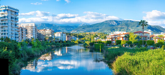 Beautiful river embankment with park area against backdrop of picturesque mountains in city of Alanya, Turkey. Colorful panoramic landscape.