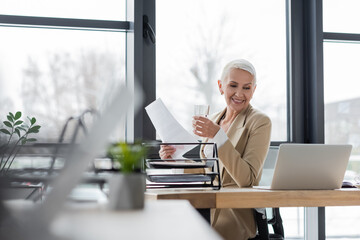 successful banker with documents and glass of water smiling during online conference on laptop.