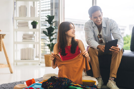Young adult southeast asian couple getting ready for holidays travel trip pack suitcase and using digital tablet
