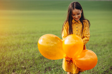 Little girl with yellow balloons in the field
