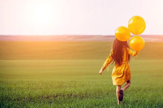 Little girl with yellow balloons in the field