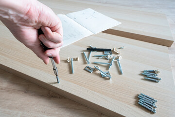 Male right hand and parts of unfinished furniture , metal screws and tools lying on the floor with...