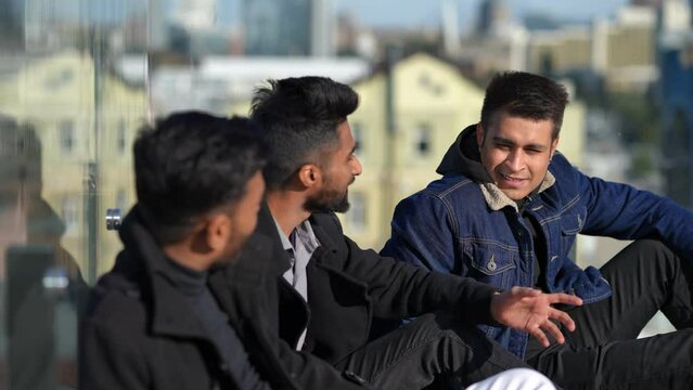 Smiling Middle Eastern man sitting with friends on rooftop talking enjoying weekend leisure. Portrait of confident young handsome guy celebrating bachelor party with mates. Happiness concept