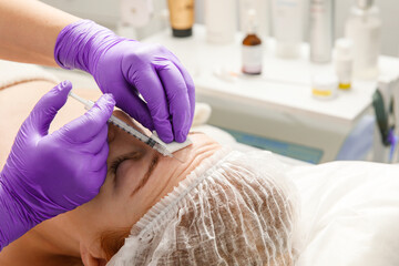 A cosmetologist performs a procedure of rejuvenating injections for the face to tighten and smooth out wrinkles on the skin of a woman's face. Cosmetic skin care in a beauty salon.