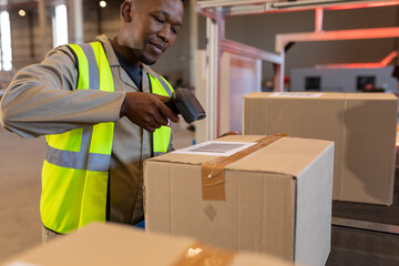 African american young male warehouse worker scanning barcode with reader on cardboard box