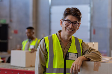 Portrait of happy asian mature man standing by box with african american male coworker in background