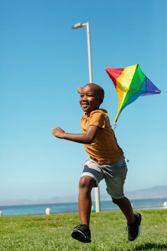 Happy african american boy running with colorful kite against clear blue sky with copy space