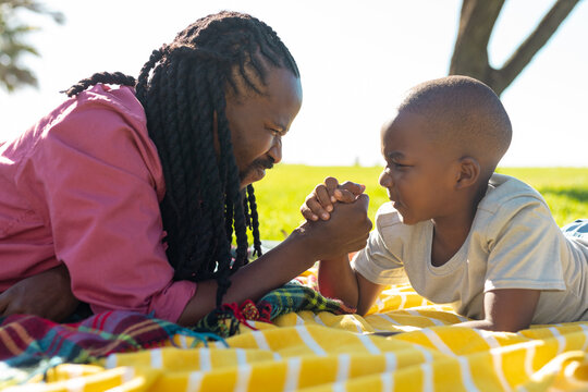 African american father and son enjoying arm wrestling on picnic blanket at park on sunny day