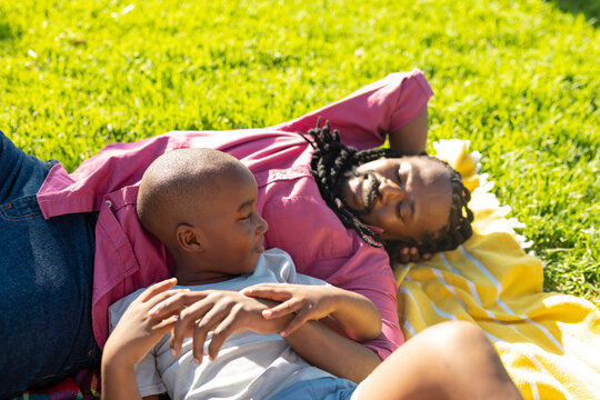 High angle view of african american father and son lying on picnic blanket at park during sunny day
