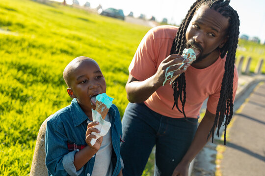 African american father and son eating melting ice cream on sunny day