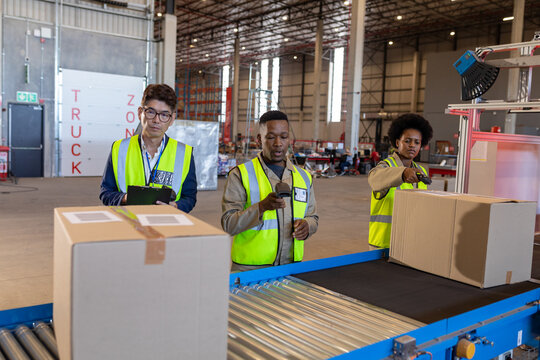 Asian male manager standing with african american workers scanning cardboard boxes on conveyor belt