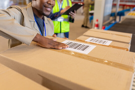 Midsection of african american young male worker labelling barcode on cardboard box in warehouse