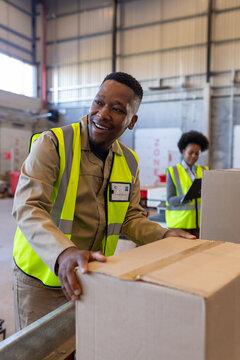 Smiling african american young man with cardboard box looking away and female coworker in background