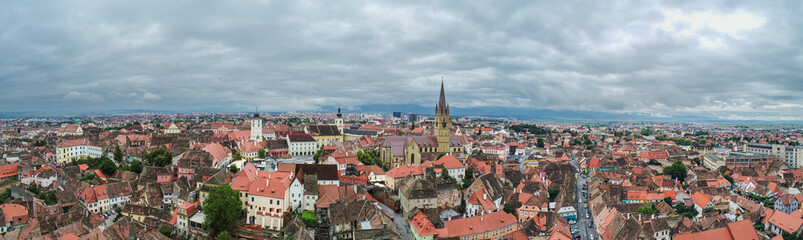 Naklejka na ściany i meble Landmarks of Romania. Aerial view of the old center of Sibiu city at the bottom of Fagaras Mountains during a cloudy sky day. Evangelical Cathedral in frame.