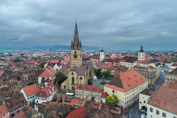 Fototapeta na wymiar Landmarks of Romania. Aerial view of the old center of Sibiu city at the bottom of Fagaras Mountains during a cloudy sky day. Evangelical Cathedral in frame.