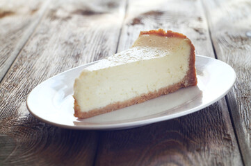 A piece of cheesecake lies in a white plate on a wooden table. Breakfast