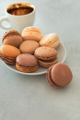 Plate with macaron cake and coffee cup on a gray background. Confectionery - nut-chocolate macrons. Sweet breakfast, dessert. Vertical photo with copy space.