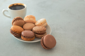 Plate with macaron cake and coffee cup on a gray background with copy space. Confectionery - nut-chocolate macrons. Sweet breakfast, dessert