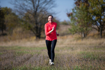 Fototapeta premium Cheerful athletic senior woman. Positive elderly woman is doing a jog. Portrait of a sporty elderly woman in the park