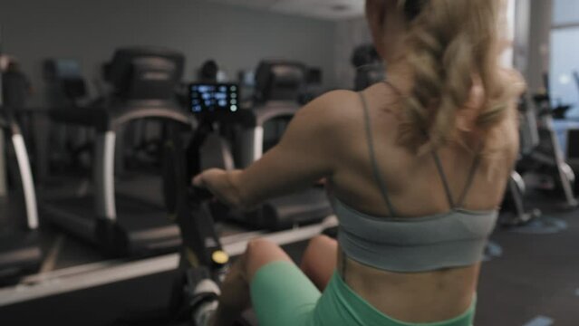 Back view of woman exercising on rowing machine. Shot with RED helium camera in 8K. 