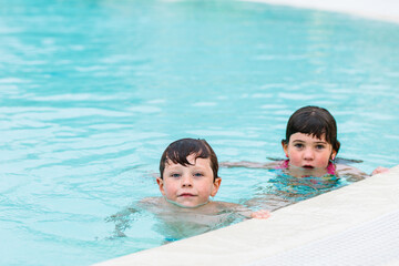 Cute little siblings swimming in pool on summer day