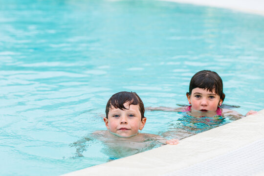 Cute little siblings swimming in pool on summer day