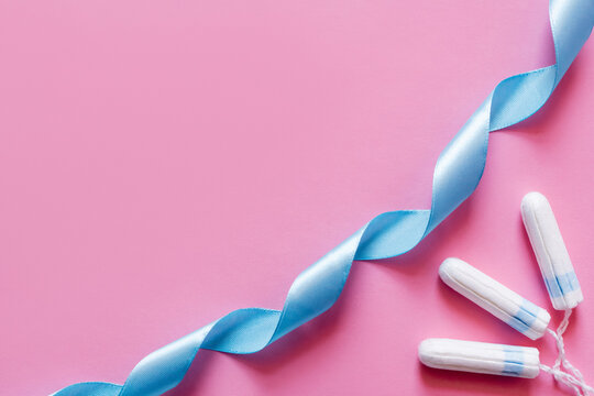 top view of blue satin ribbon near tampons on pink background.