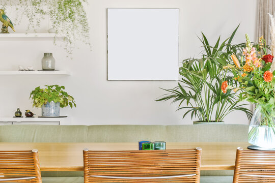 Wooden dining table with chairs in light room decorated with plants